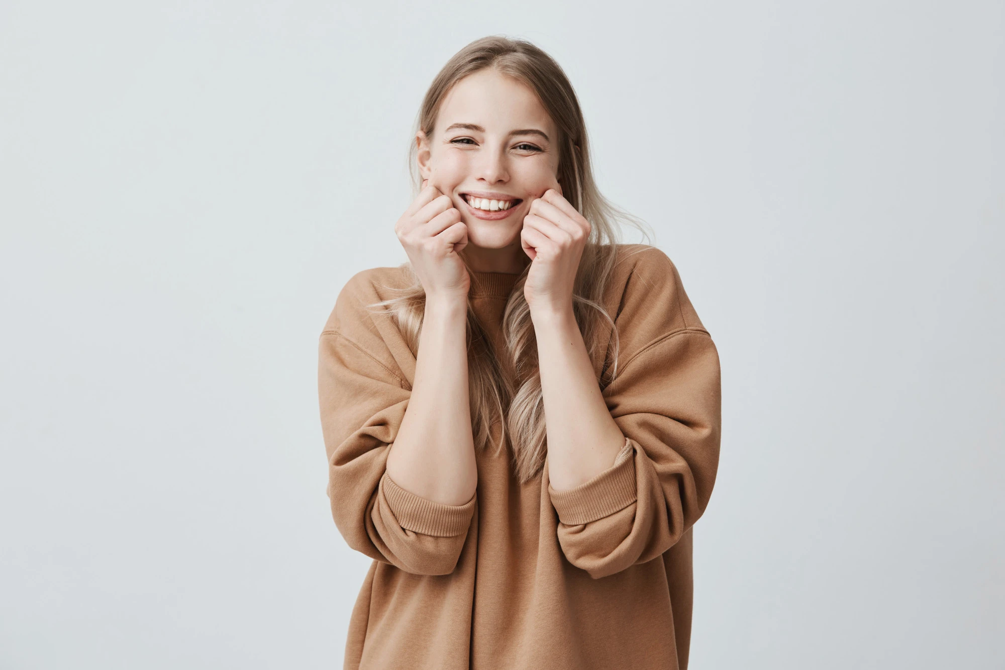 Gratitude Practice and Happiness: 7 Ways Thankfulness Boosts Your Mood charming beautiful female model smiling broadly wearing brown sweater pinching her cheeks mocking having good mood fun positive emotions feelings