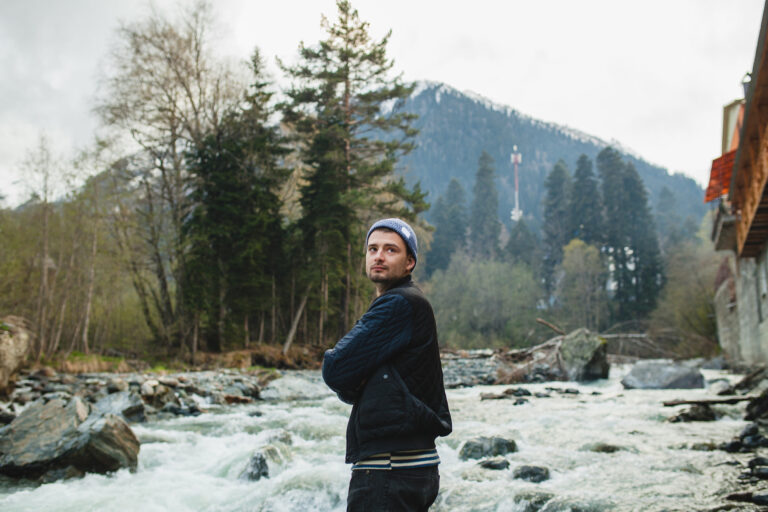 young hipster man walking rock river winter forest